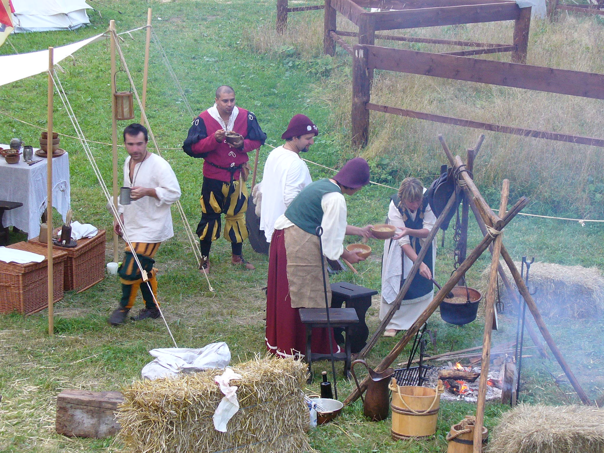 Kasdienybės istorijos rekonstrukcija. Nuotrauka, kurioje žmonės gamina valgyti lauke, apsirengę tautiniais drabužiais